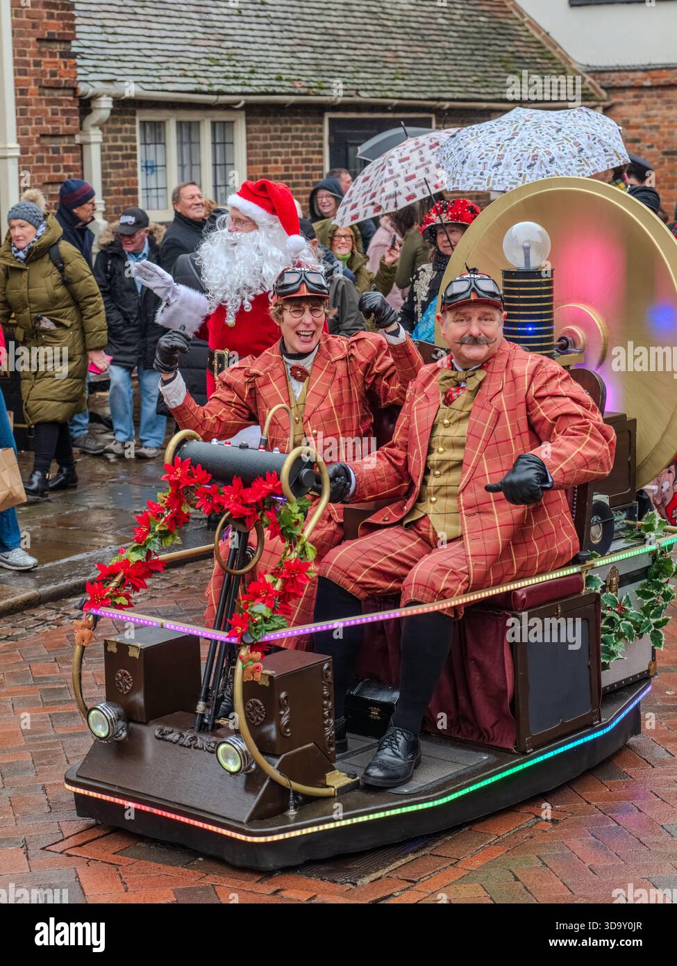 Dickens Christmas Festival Rochester UK Dezember 2025. Steampunk-Duo in roter Karo-Fahrzeit-Maschine schweben mit Lichtern, Poinsettias und Santa Parade Stockfoto