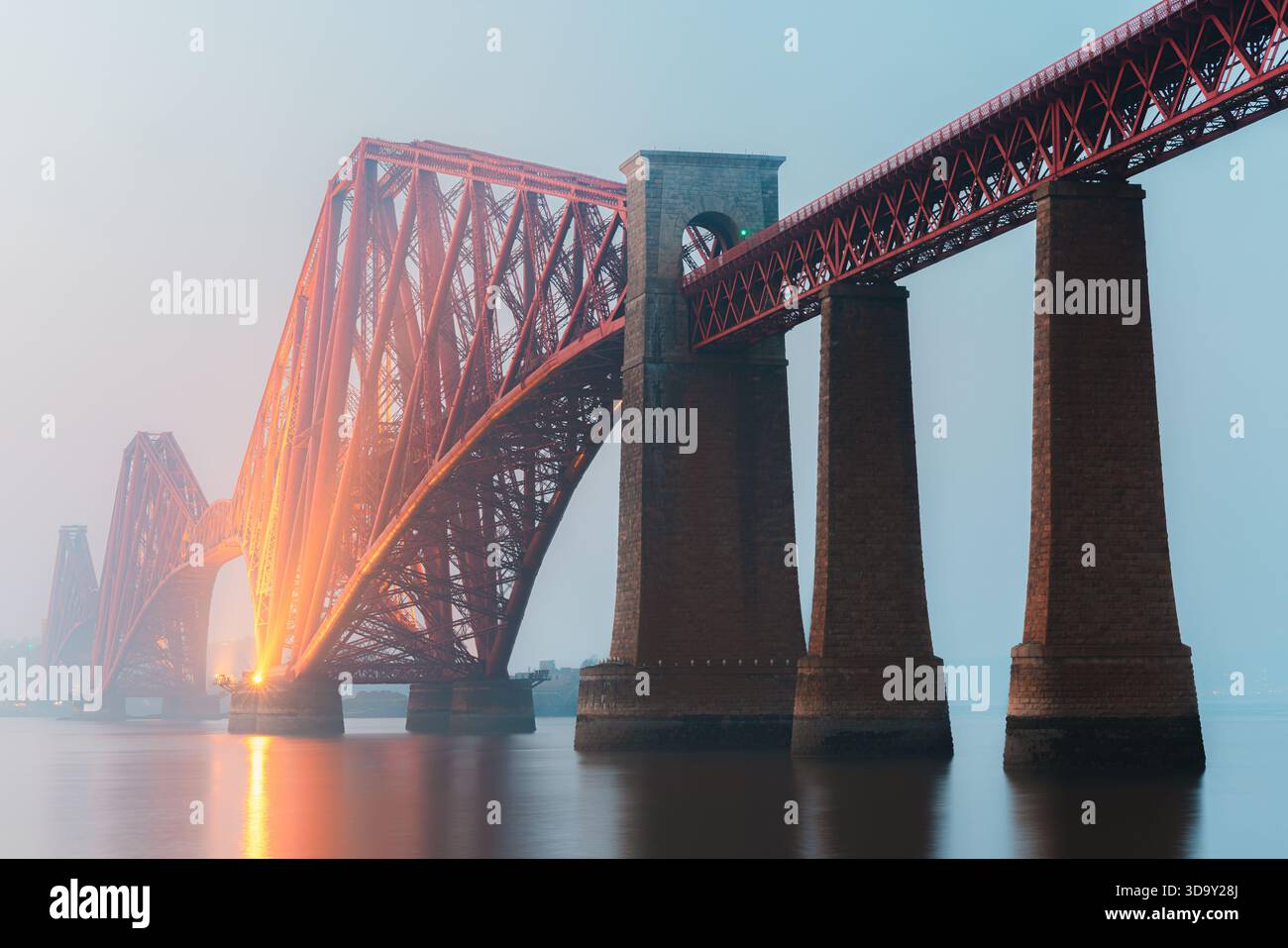 Die berühmte Forth Bridge erstreckt sich über das ruhige Wasser des Firth of Forth in der Nähe von South Queensferry in Schottland, deren rote Freischwinger durch die glühende Landschaft glühen Stockfoto