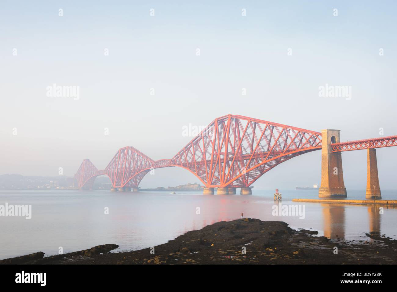Die berühmte Forth Bridge erstreckt sich über das ruhige Wasser des Firth of Forth in der Nähe von South Queensferry in Schottland, deren rote Freischwinger durch die glühende Landschaft glühen Stockfoto