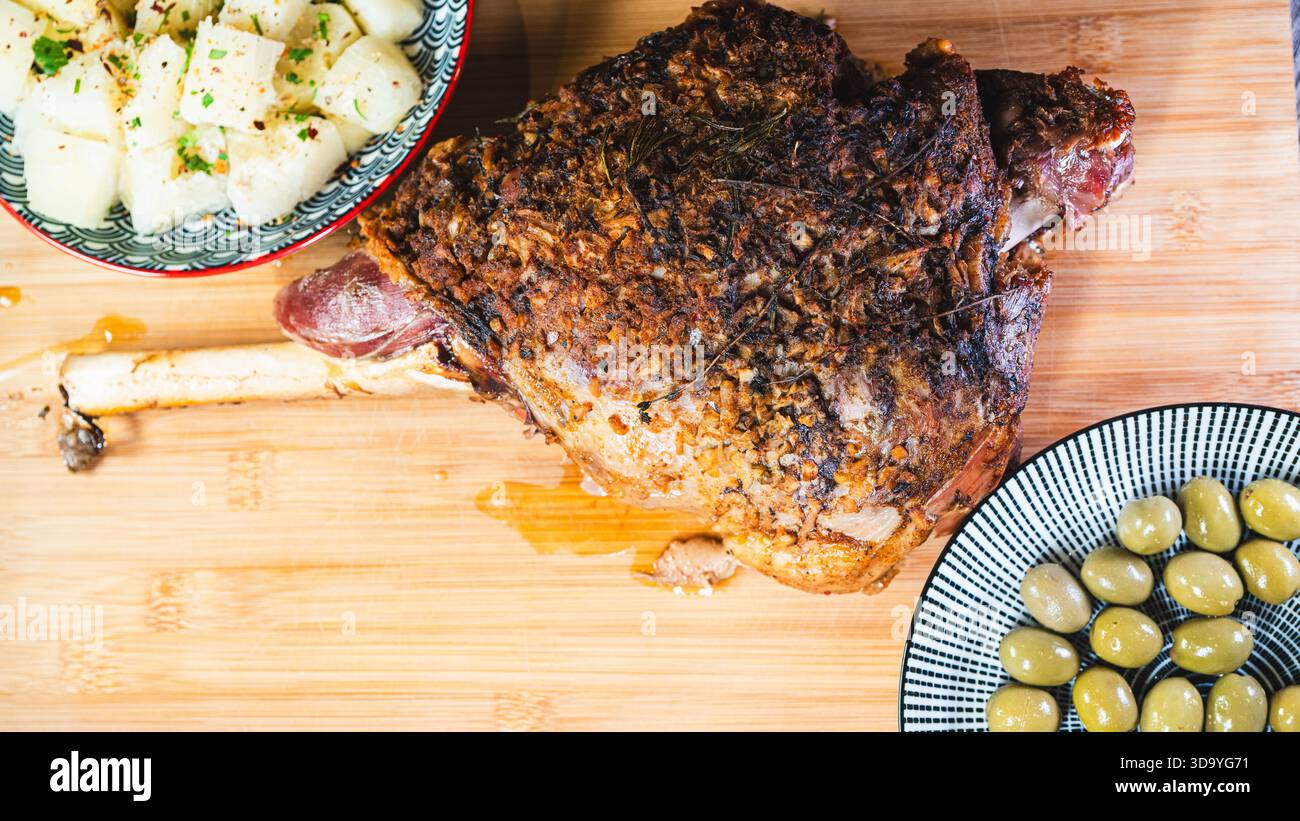 Gebratene Lammkeule auf einem Brett mit Beilagen: Oliven und Maniok-Pommes. Golden, gewürzt, perfekt für ein komplettes und herzhaftes festliches Essen. Stockfoto