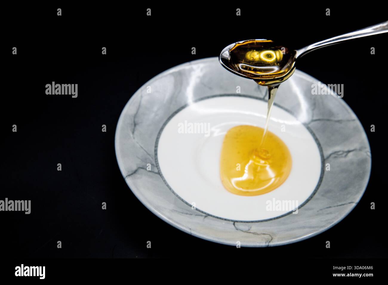 Nahaufnahme von goldenem Honig, der von einem Löffel vor dunklem Hintergrund in eine Schüssel tropft, wodurch ein reichhaltiges, appetitliches Detail entsteht. Stockfoto