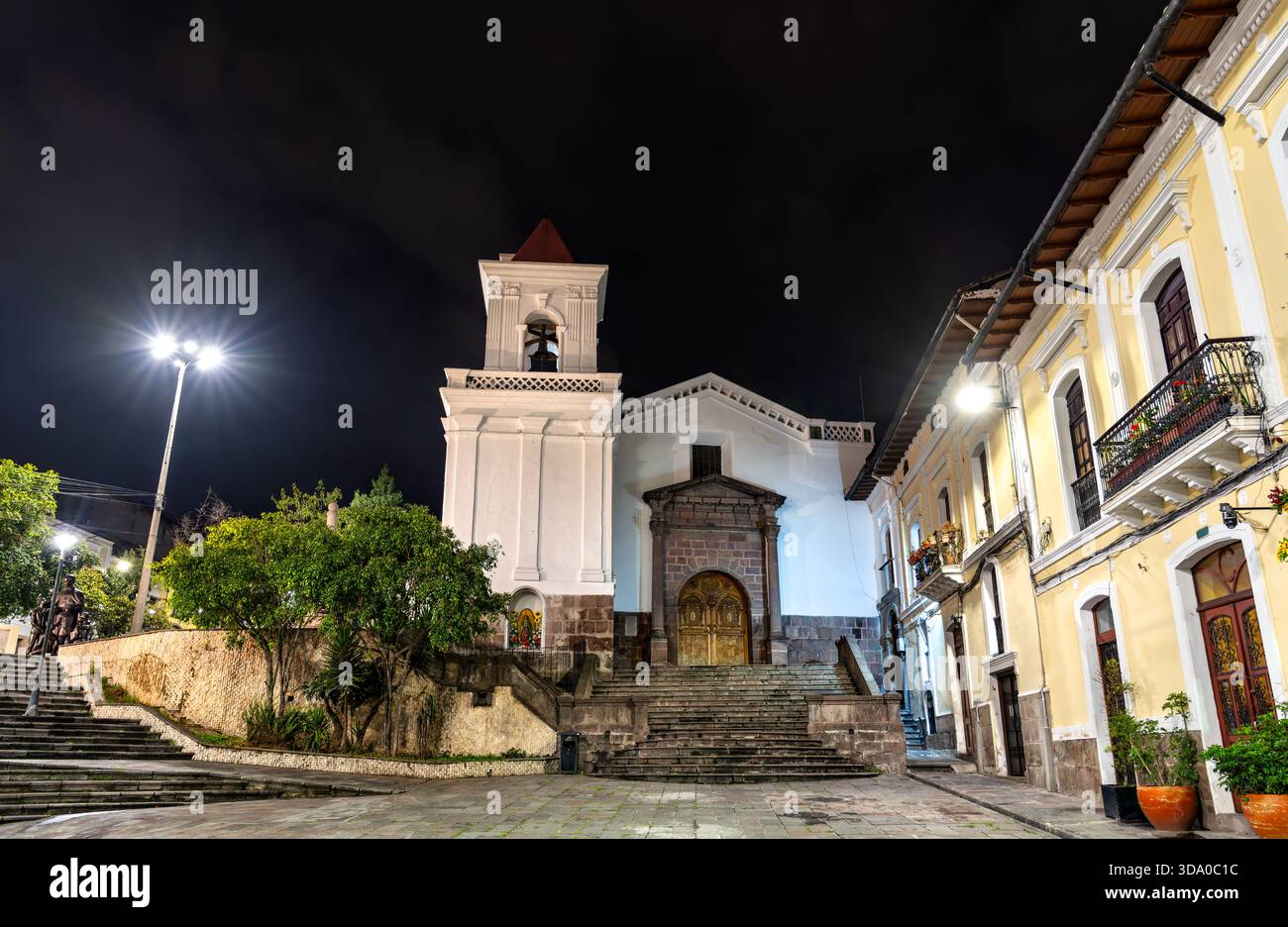 Die Kirche San Blas befindet sich in der Nähe des historischen Zentrums von Quito, Ecuador. Die weiße katholische Kirche im Kolonialstil verfügt über einen Steineingang und einen Glockenturm, der unter dem Nachthimmel beleuchtet ist Stockfoto