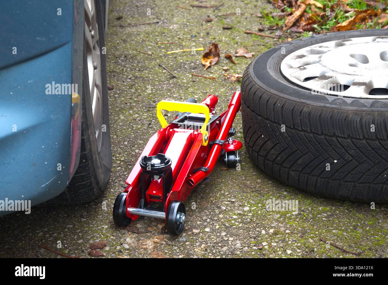 An einem Fahrzeug wird mit Wagenheber und Reserverad gearbeitet, wahrscheinlich aufgrund eines Reifenpangels Stockfoto