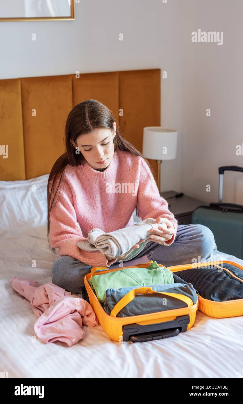 Junge Frau faltet Kleidung, packt Koffer für eine Reise auf einem Hotelbett Stockfoto