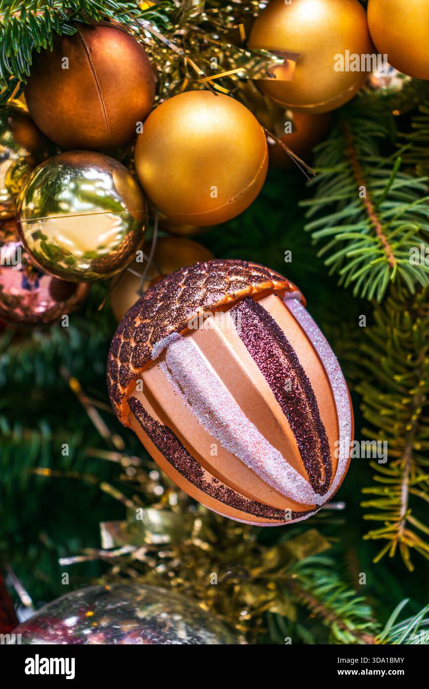 Nahaufnahme des goldenen Weihnachtsschmucks, der an einem verzierten Tannenbaum mit festlichen Lichtern hängt. Weihnachtsdekoration für Weihnachten und Neujahr. Stockfoto