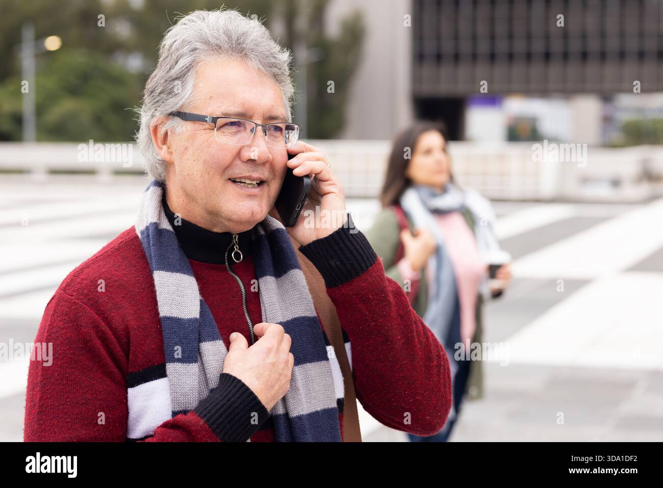 Seniorenpaar, das auf der plaza-Kreuzung läuft, Mann, der auf dem Smartphone spricht, Frau, die eine Kaffeetasse hält Stockfoto