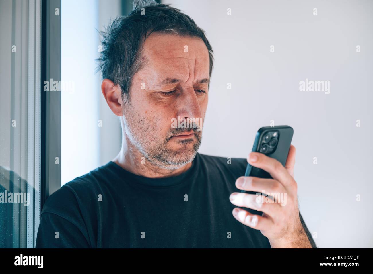 Echter Kaukasier mittleren Alters, der das Smartphone mit tiefer Trauer und Sorge anstarrt. Stress, schlechte Nachrichten, Einsamkeit, Schulden, psychische Gesundheit. Selektiver Fokus Stockfoto