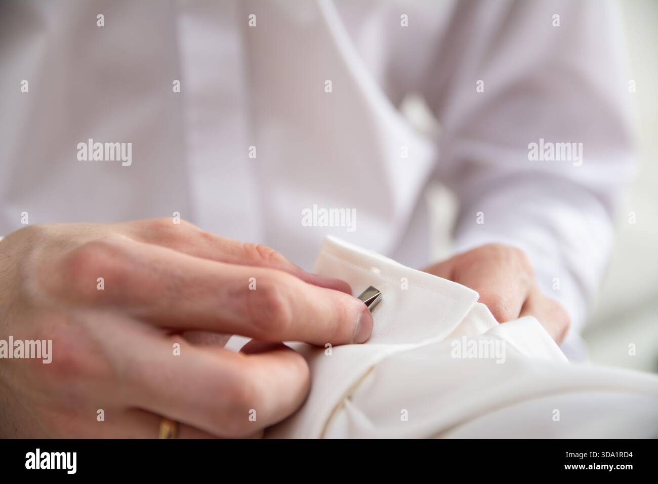 Eine Nahaufnahme der Hände des besten Mannes, die dem Bräutigam helfen, Manschettenknöpfe anzuziehen. Beide tragen weiße Hemden. Nahaufnahme von der Hochzeit Stockfoto