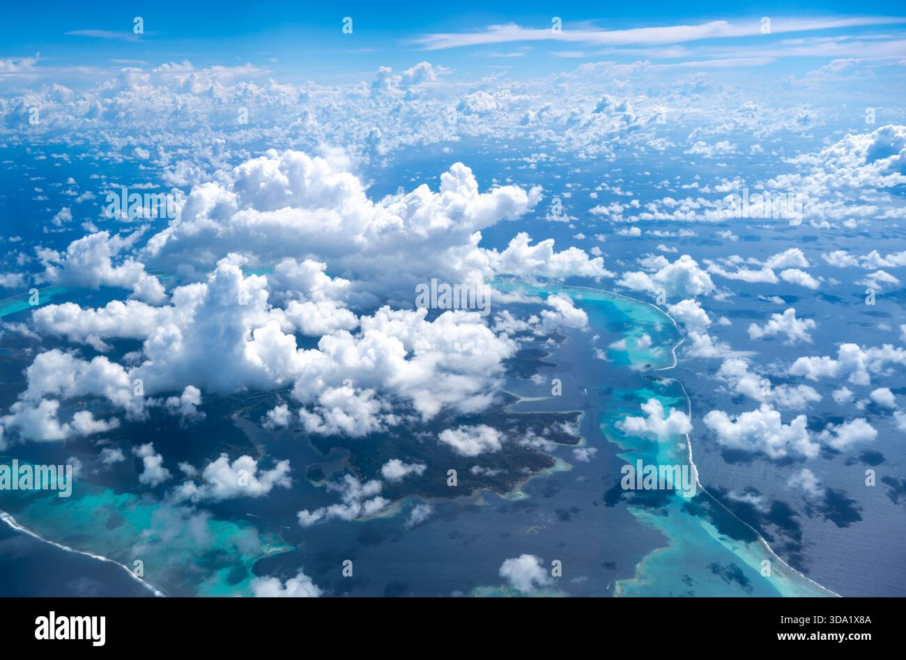 Die atemberaubende Insel Tahaa, umgeben von einer türkisfarbenen Lagune und einem Korallenriff, taucht durch verstreute Wolken im riesigen Pazifik auf. Ein Atemzug Stockfoto