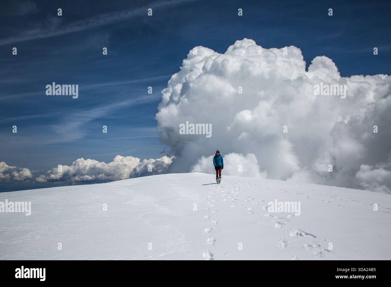 Eine Frau läuft auf einer verschneiten Bergkuppel mit großen Wolken im Hintergrund Stockfoto