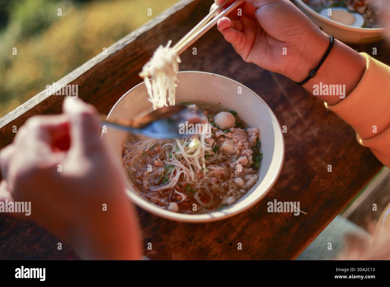 Die Person genießt köstliches asiatisches Mittagessen und isst warme Nudelsuppe aus einer Schüssel mit Essstäbchen. Diese leckere Mahlzeit ist ein beliebtes Speisenangebot für wundervolle Mahlzeiten Stockfoto
