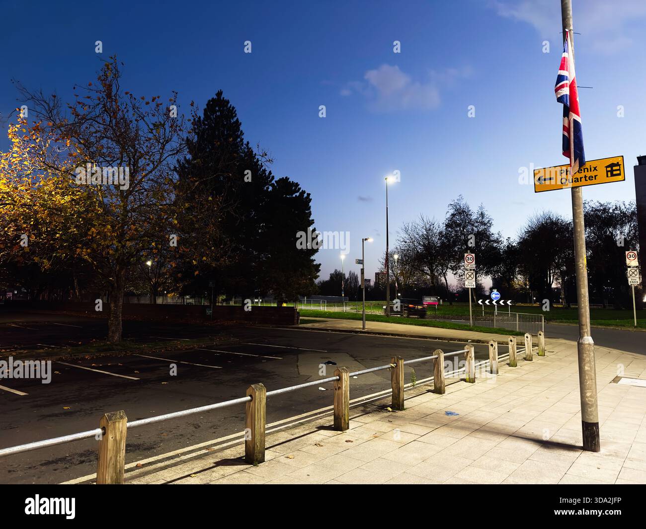 Salford, Großbritannien - 08. November 2025: Ruhiger Abend in Salford mit Park, Fahnenmast, Straßenlaternen und Verkehrsschildern. Stockfoto