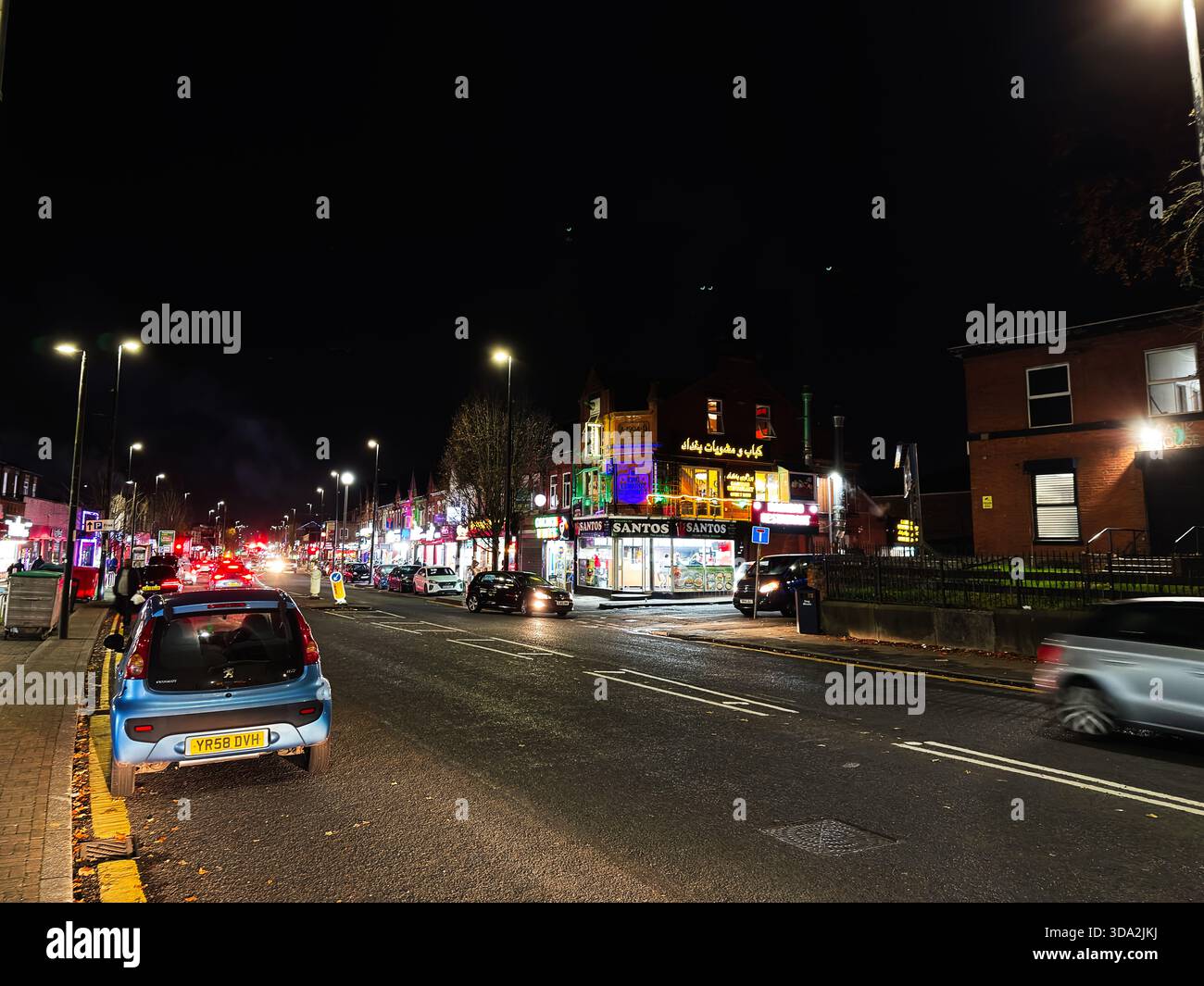 Salford, Großbritannien - 8. November 2025: Nachtszene auf einer lebhaften Salford Street mit Neonschildern, Verkehr und Fußgängern. Stockfoto