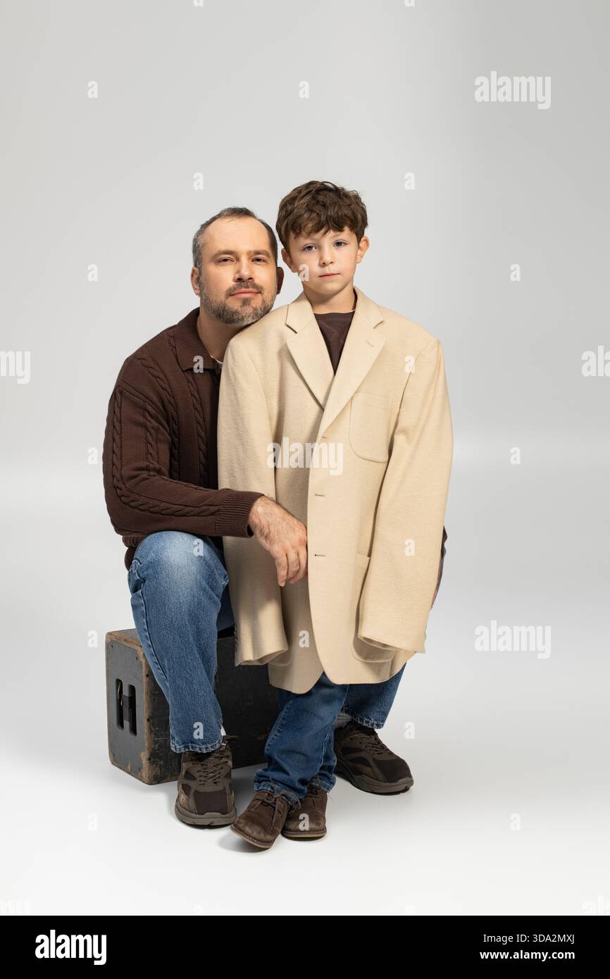 Ein Mann und sein Sohn posieren zusammen, der Junge humorvoll in einem übergroßen Blazer. Stockfoto