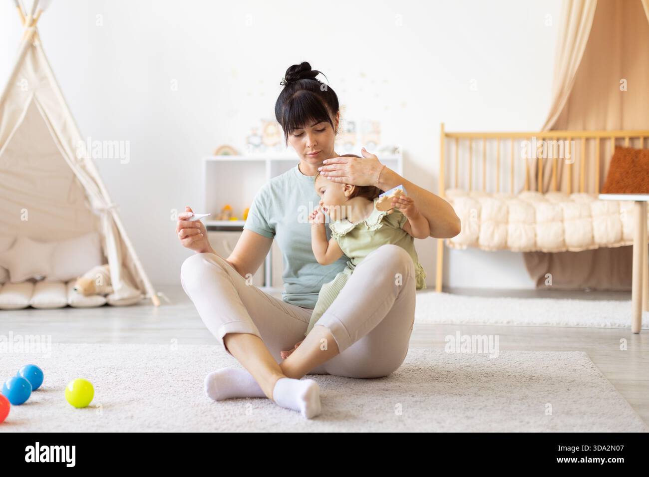 Mutter kontrolliert die Temperatur des Babys mit sanfter Sorgfalt, während sie das Thermometer hält Stockfoto