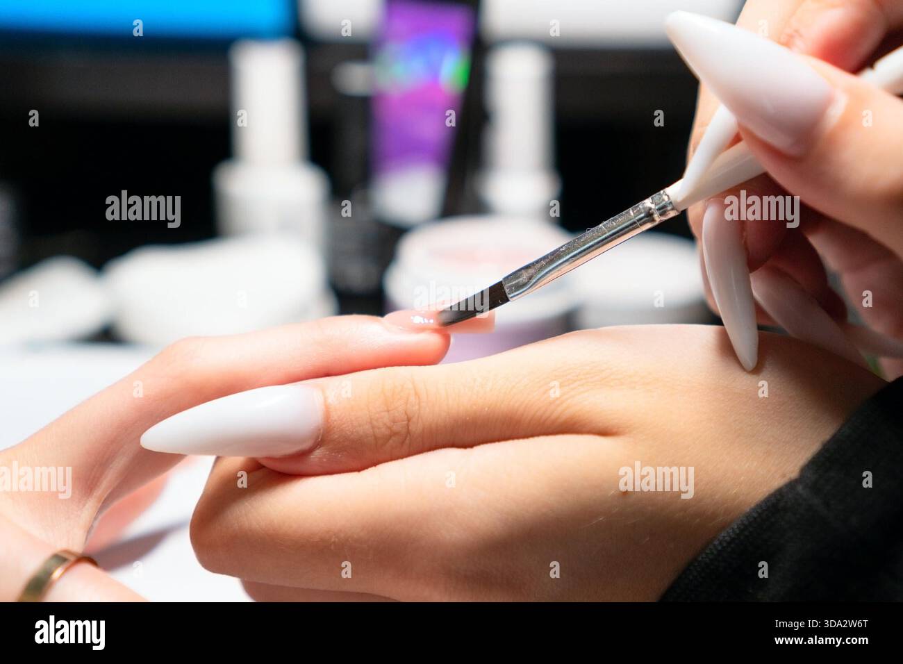 Professionelle Maniküre tragen bei der Nagelverlängerung sorgfältig gellack auf, um eine perfekte, gleichmäßige Abdeckung und Form zu gewährleisten. Stockfoto
