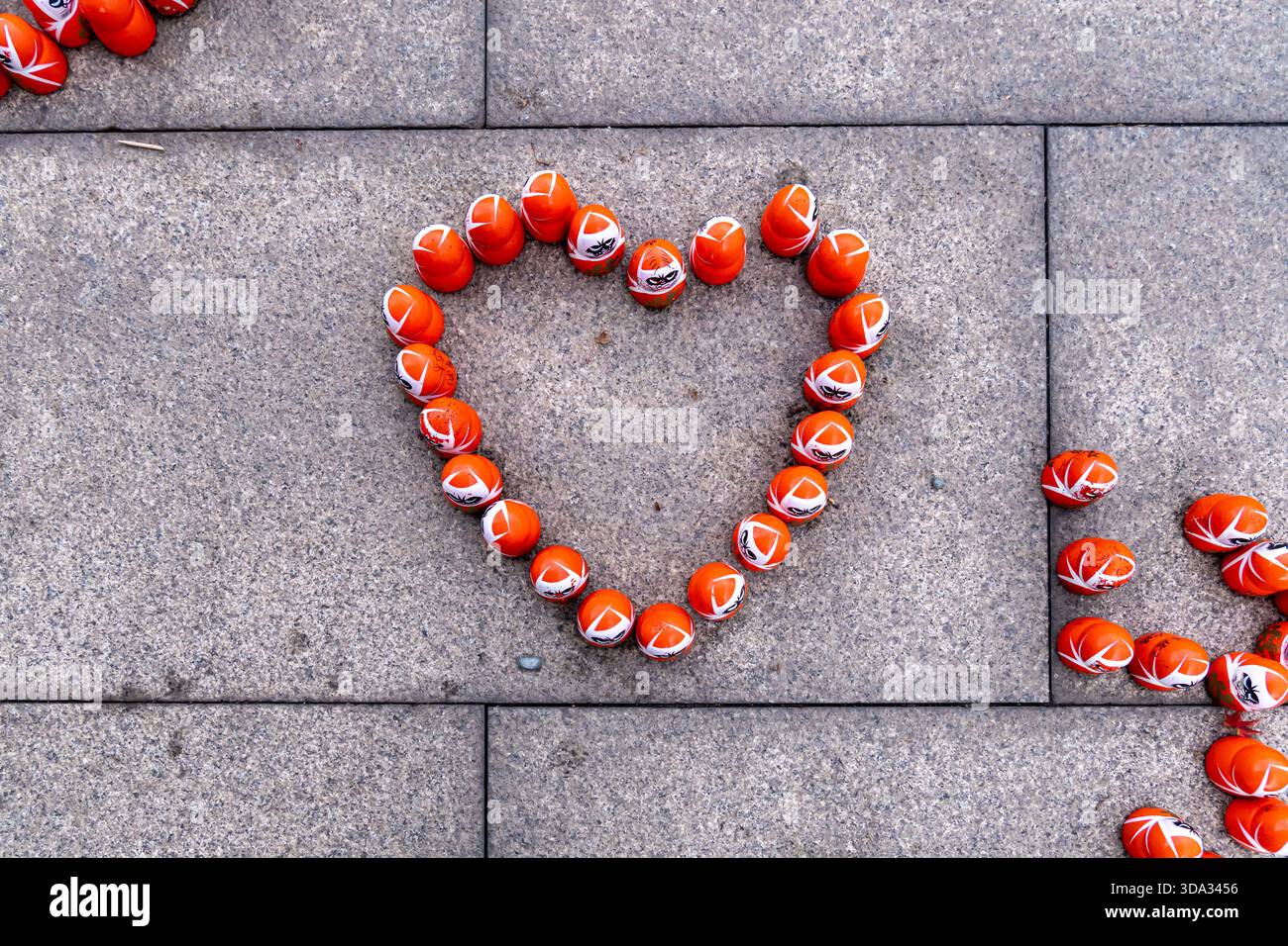 Orangefarbene Kugeln sind in Herzform auf einer grauen Steinoberfläche angeordnet. Die Szene zeigt Kreativität mit einfachen Objekten in einem urbanen Außenbereich. Stockfoto