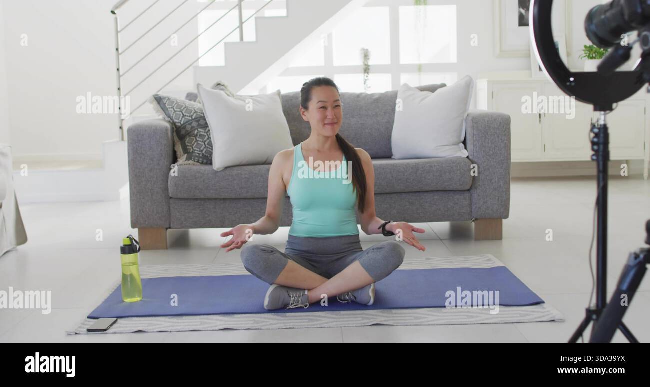 Sitzende Frau mit Minztank, Handflächen auf blauer Yogamatte zu Hause, Ringlichtaufnahme Stockfoto