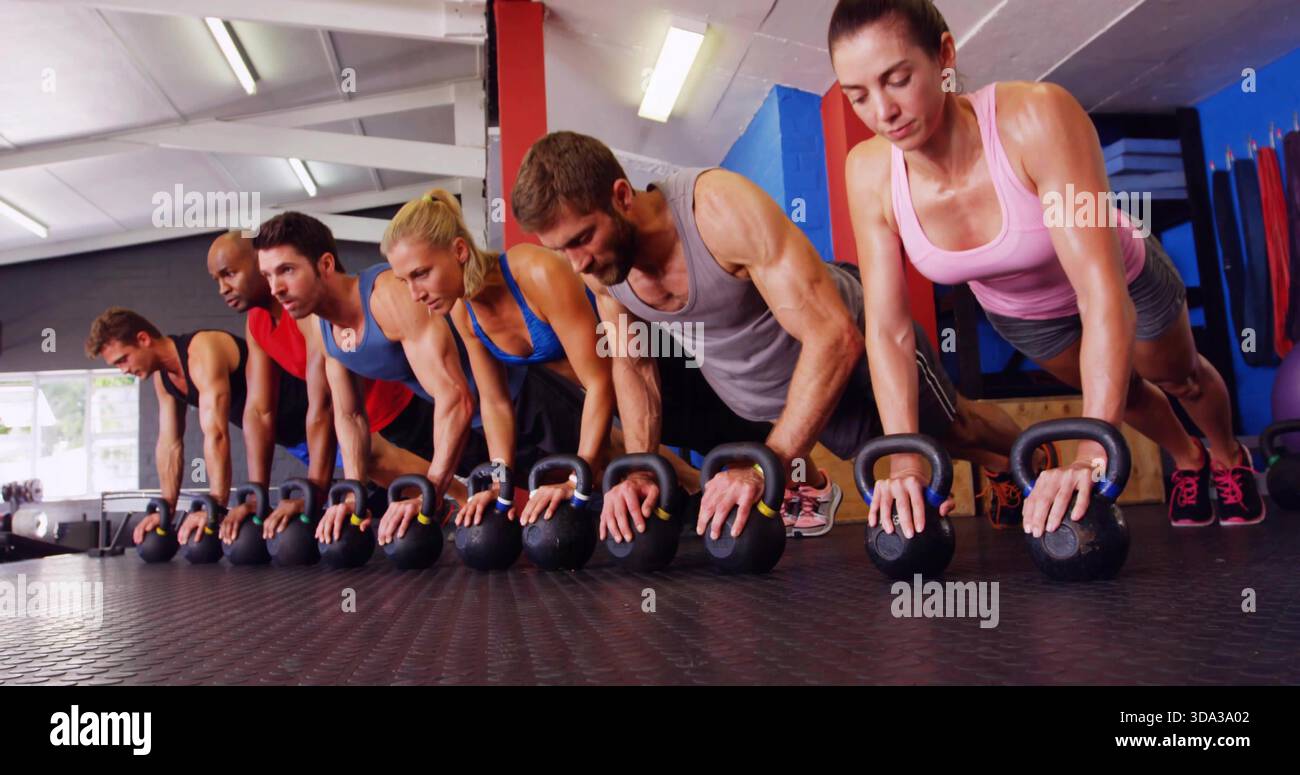 Halten Sie eine Gruppe von sechs Erwachsenen, die Kettlebells greifen, während Sie eine Plank im Fitnessstudio ausführen und Aktivkleidung zeigen Stockfoto
