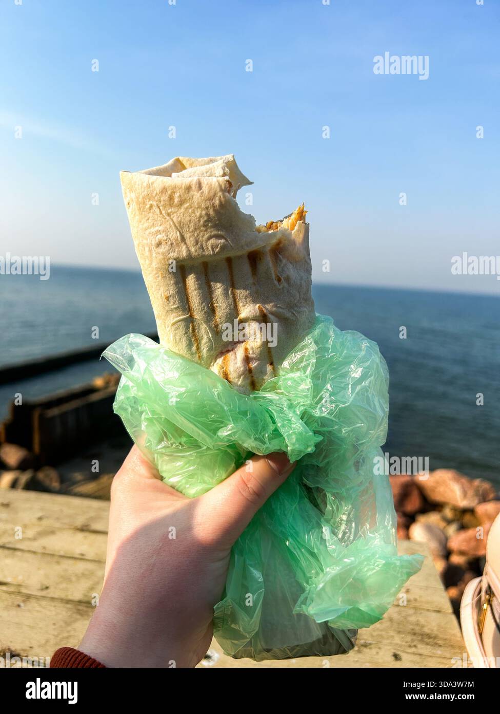 Die Frau hält Shawarma Wrap Kebab in Händen vor dem Meer. Street-Food-Konzept. Essen gehen. Essen unterwegs. Shawarma in Lavash. Praktisches Essen. Stockfoto