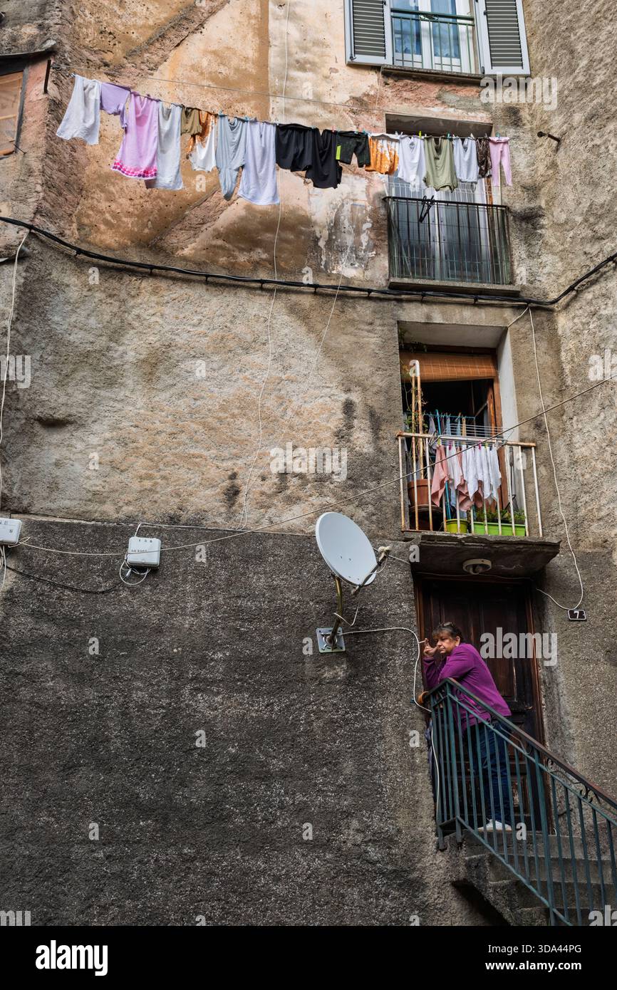 Eine Einwohnerin raucht eine Zigarette auf den Stufen ihres Wohnhauses in der Altstadt von Corte, Korsika, Frankreich Stockfoto