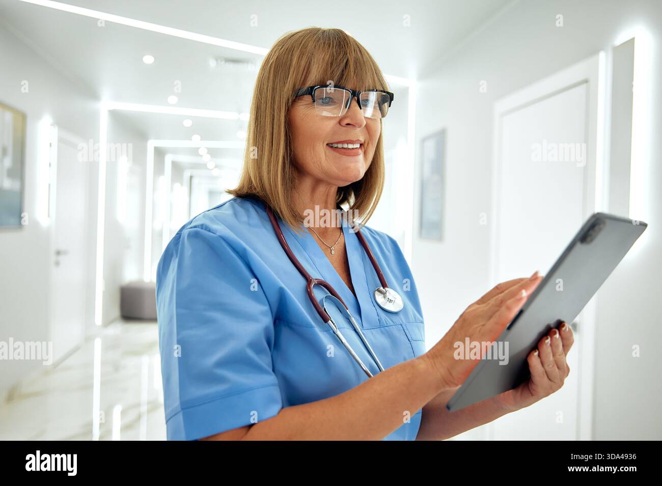 In einem hellen und modernen Krankenhausflur interagiert eine freundliche Krankenschwester mit blauen Peelings mit einer Tablette und demonstriert ihr Mitgefühl und p Stockfoto