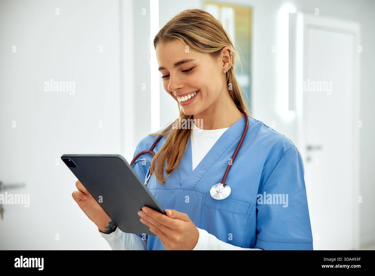 In einem hellen und modernen Krankenhausflur interagiert eine freundliche Krankenschwester mit blauen Peelings mit einer Tablette und demonstriert ihr Mitgefühl und p Stockfoto