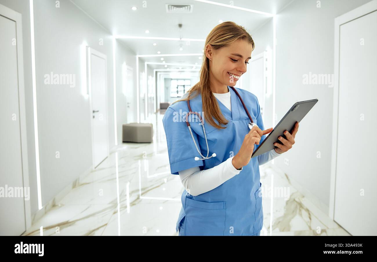 In einem hellen und modernen Krankenhausflur interagiert eine freundliche Krankenschwester mit blauen Peelings mit einer Tablette und demonstriert ihr Mitgefühl und p Stockfoto