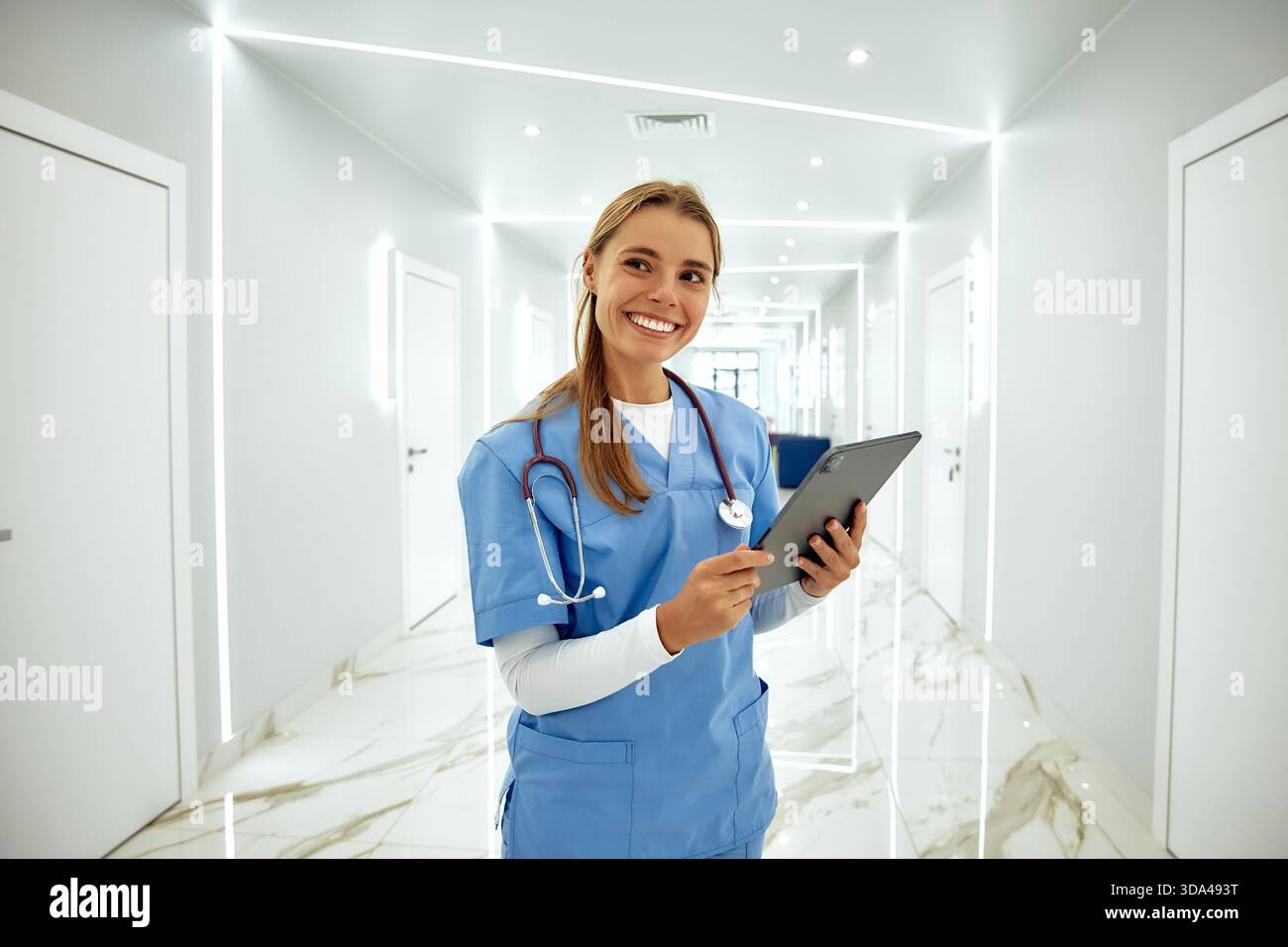 In einem hellen und modernen Krankenhausflur interagiert eine freundliche Krankenschwester mit blauen Peelings mit einer Tablette und demonstriert ihr Mitgefühl und p Stockfoto