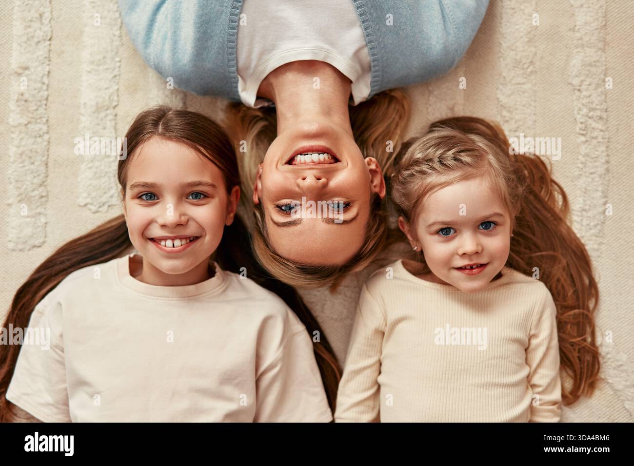 Eine lächelnde Mutter und Töchter genießen einen Moment der Freude auf einem weißen Teppich und zeigen Familienverbundenheit und Glück in einer gemütlichen Umgebung voller Wärme A Stockfoto