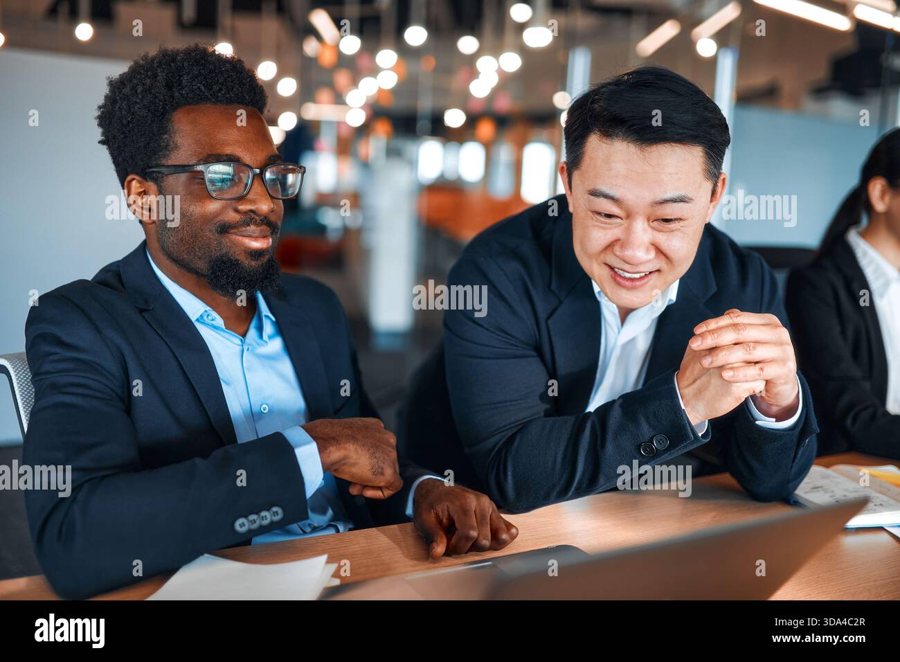 Ein Team junger Geschäftsleute in formellen Anzügen, die in einem modernen Büro mit Laptops arbeiten. Mitarbeiter, die einen Arbeitsplan oder ein Projekt besprechen Stockfoto