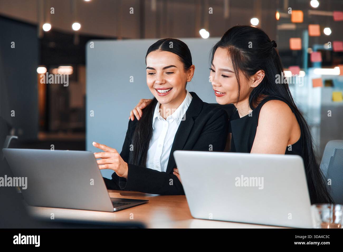 Ein Team junger Geschäftsleute in formellen Anzügen arbeitet mit Laptops, während sie in einem modernen Büro sitzen. Geschäftsfrauen, die an Laptops arbeiten und über ein Bu diskutieren Stockfoto