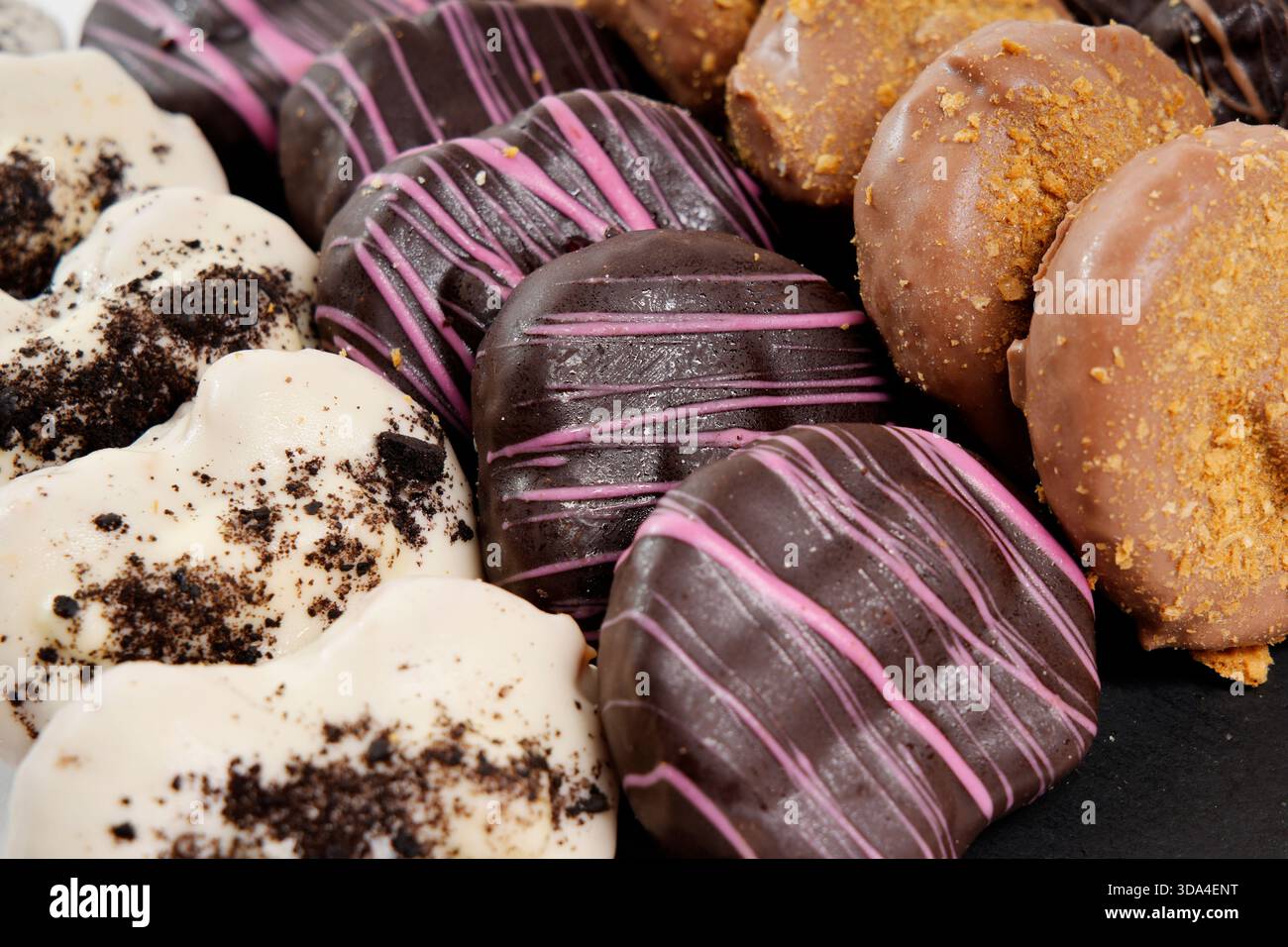 Herzförmige Donuts mit Schokoladen-, Rosa- und Cremeglasur mit Belag Stockfoto