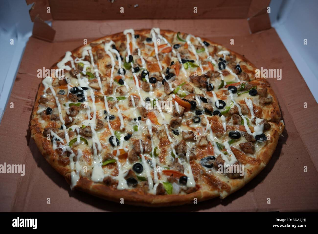 Eine köstliche hausgemachte Pizza mit verschiedenen Belägen, einschließlich Oliven, Wurst und Käse, in einer Pappschachtel, die ein herzhaftes Aroma ausstrahlt Stockfoto