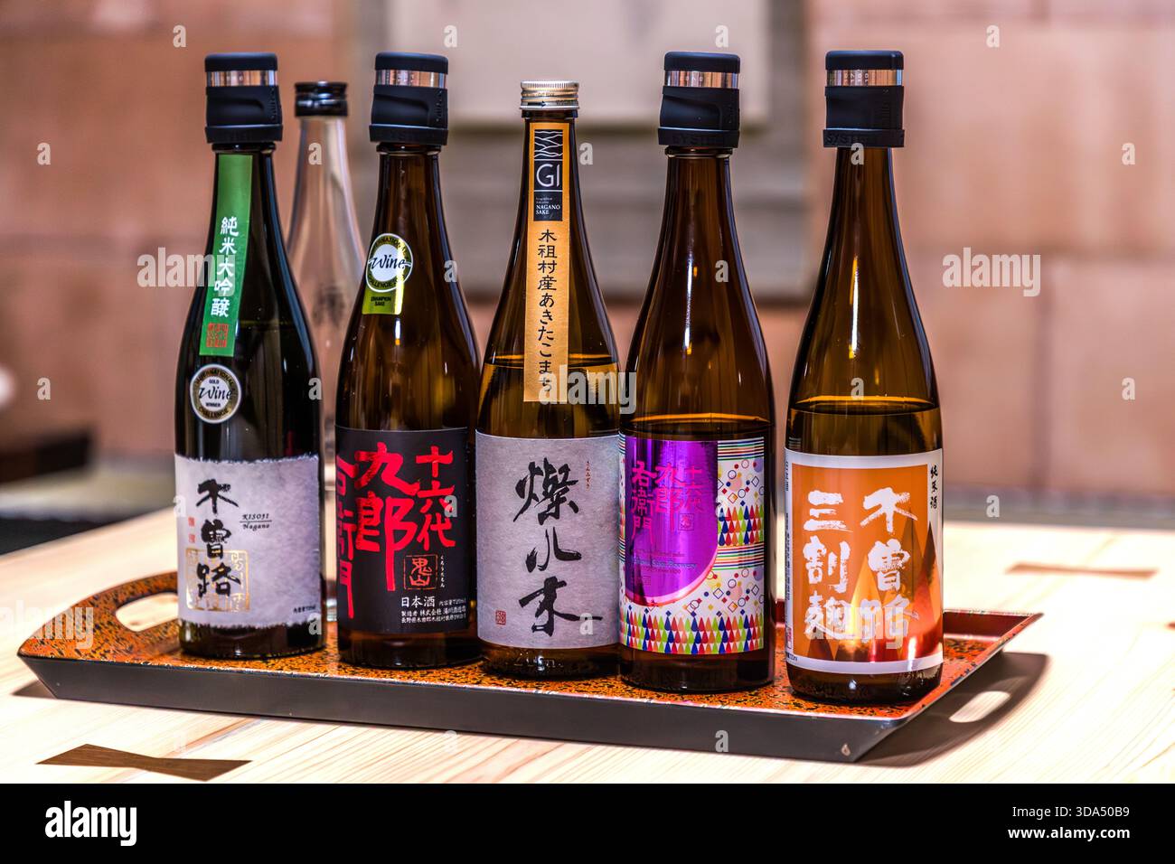 Fünf Flaschen Sake aus der Region Kisoji (木曽路) auf einem lackierten Serviertablett, darunter ein Junmai Daiginjo und andere lokale Sorten. Die Sake-Brauerei im Kiso-Tal, Präfektur Nagano, verwendet regionales Bergwasser und lokale Reissorten und verkörpert die lange Tradition der Sake-Brauerei in der Region Kiso. Kiso, Präfektur Nagano, Japan Stockfoto