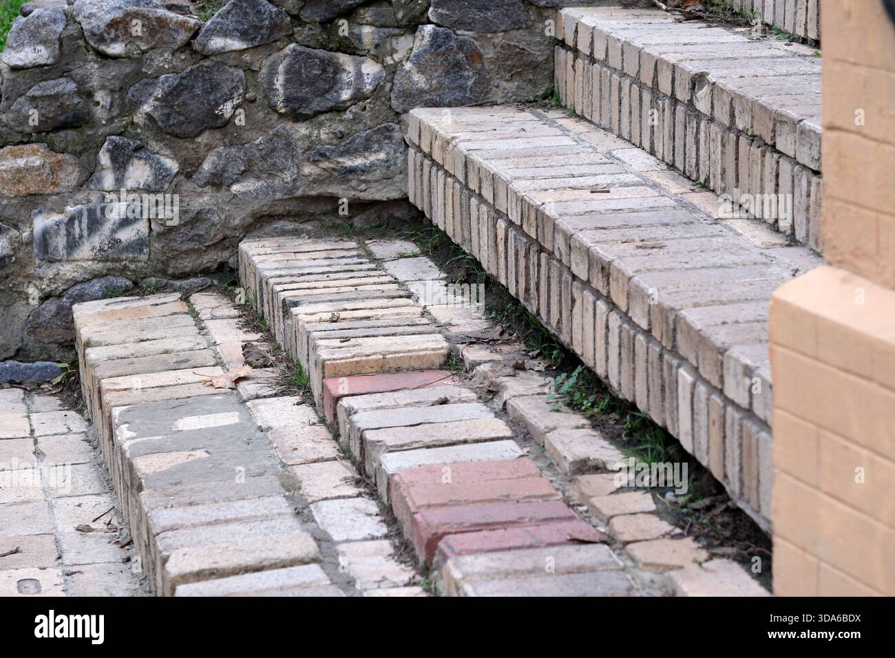 Verwitterte Ziegelsteine bilden bezaubernde Stufen, umgeben von zerklüftetem Stein und Grün. Stockfoto