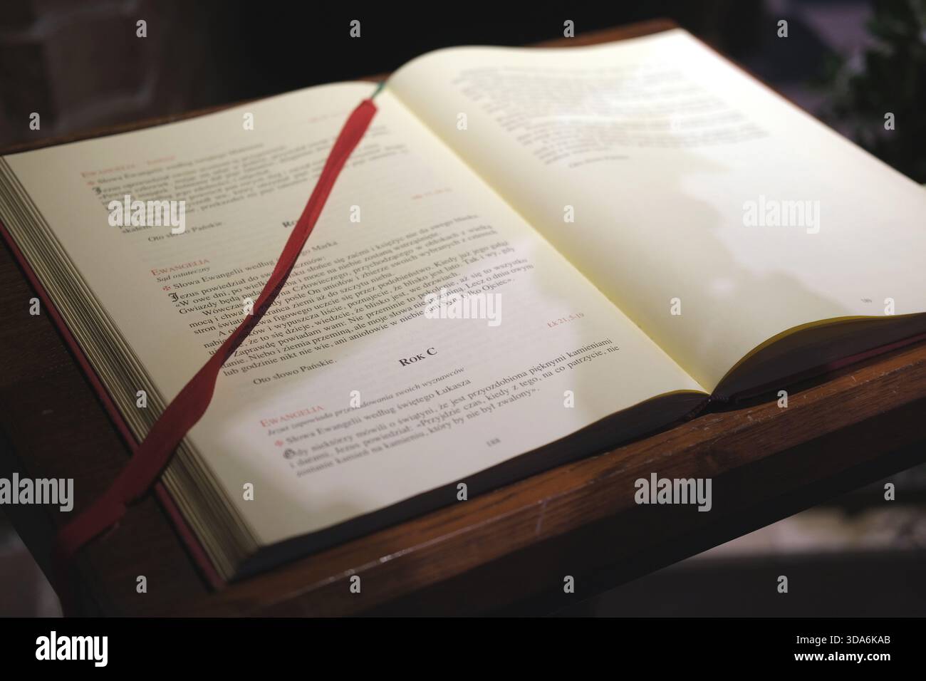 Weite Ansicht eines offenen liturgischen Buches in polnischer Sprache auf einem dunklen hölzernen Rednerpult, cremefarbene Papierseiten mit schwarzem und rotem Text, Lesezeichen mit rotem Band. Stockfoto