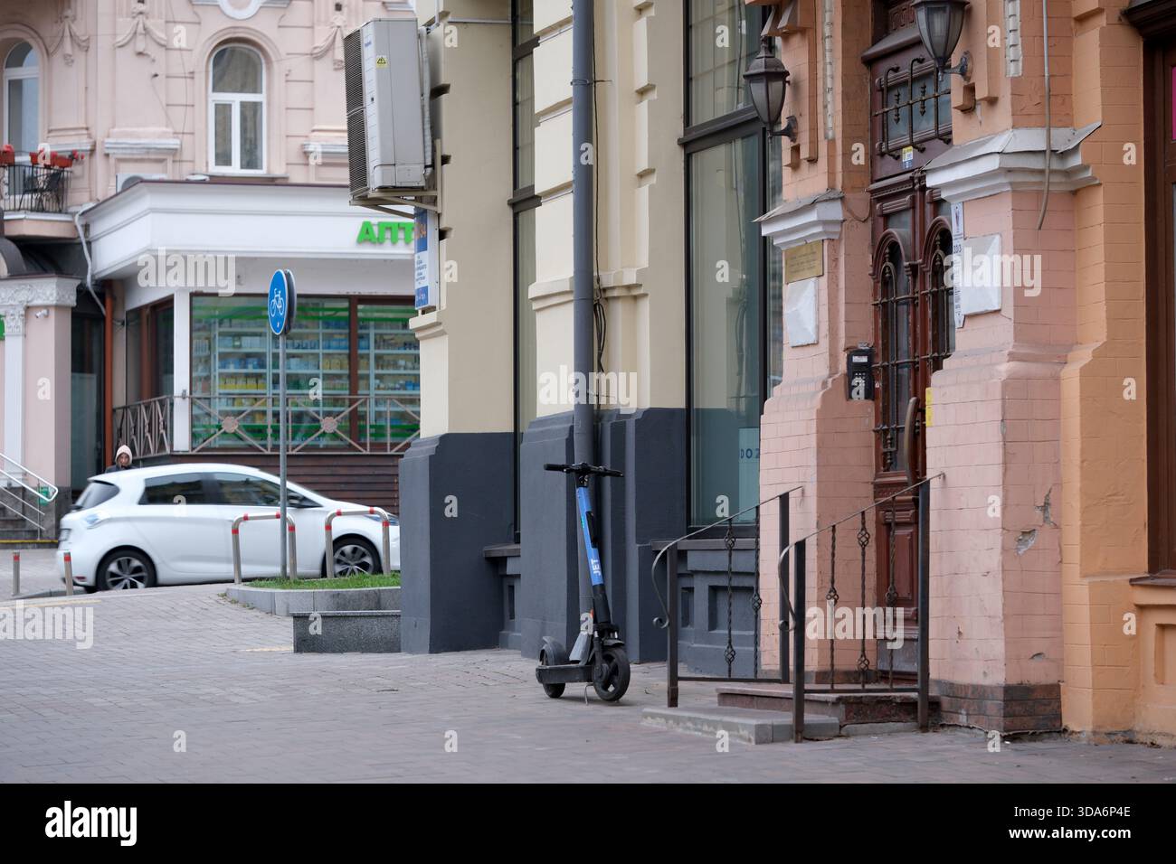 Ein einsamer Elektroroller steht an einem eleganten Eingang, während ein Auto vorbeifährt. Kiew, Ukraine. Dezember 2025. Stockfoto