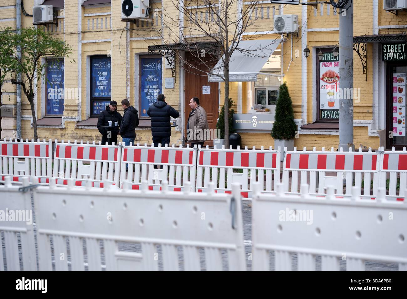 Eine Gruppe von vier Personen unterhält sich in der Nähe einer Baustelle in einer Stadt. Kiew, Ukraine. Dezember 2025. Stockfoto