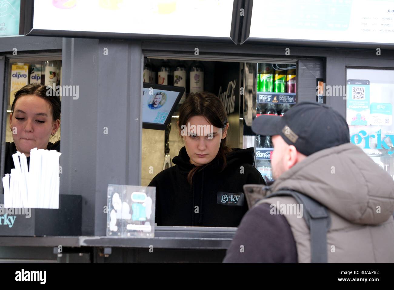 Zwei aufmerksame Mitarbeiter servieren während einer lebhaften Veranstaltung Getränke an einem belebten Stand. Kiew, Ukraine. Dezember 2025. Stockfoto