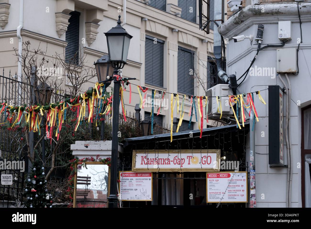 Festliche Bänder erhellen die Straßen der Stadt tagsüber vor einer belebten Bar. Andrejewski Uzviz, Kiew, Ukraine. Dezember 2025. Stockfoto