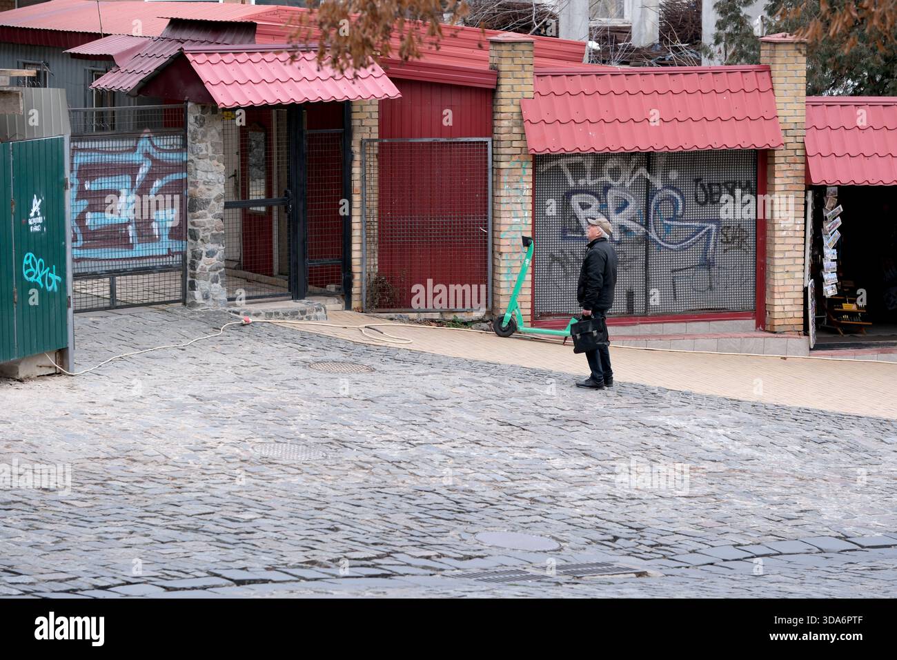 Eine Person steht auf einem Kopfsteinpflasterweg in der Nähe lebendiger Gebäude mit Graffiti. Andrejewski Uzviz, Kiew, Ukraine. Dezember 2025. Stockfoto