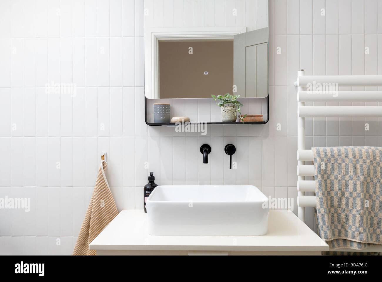 Modernes minimalistisches Badezimmer mit weiß gefliesten Wänden, Wandwaschbecken, schwarzen Armaturen und Spiegelschrank im skandinavischen Design Stockfoto