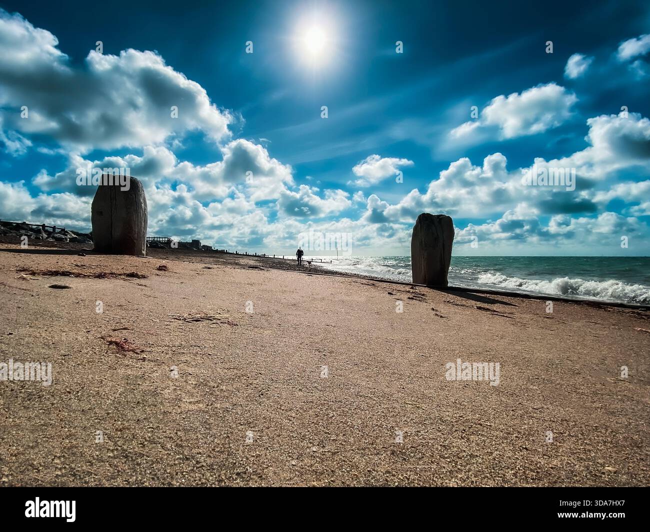 Ein einzelner Hundespazierer am Worthing Beach unter einem hellblauen Himmel mit flauschigen Wolken Stockfoto
