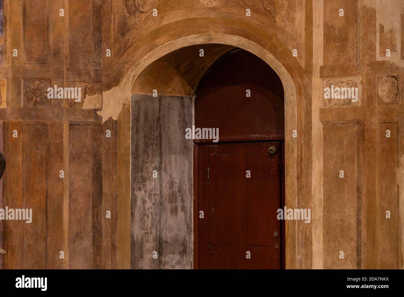 Alte bogenförmige Tür in einem historischen Steingebäude mit verblassten dekorativen Wanddetails, Boulogne-sur-Mer. Verwitterte Holztür in einem alten Bogengang. Stockfoto