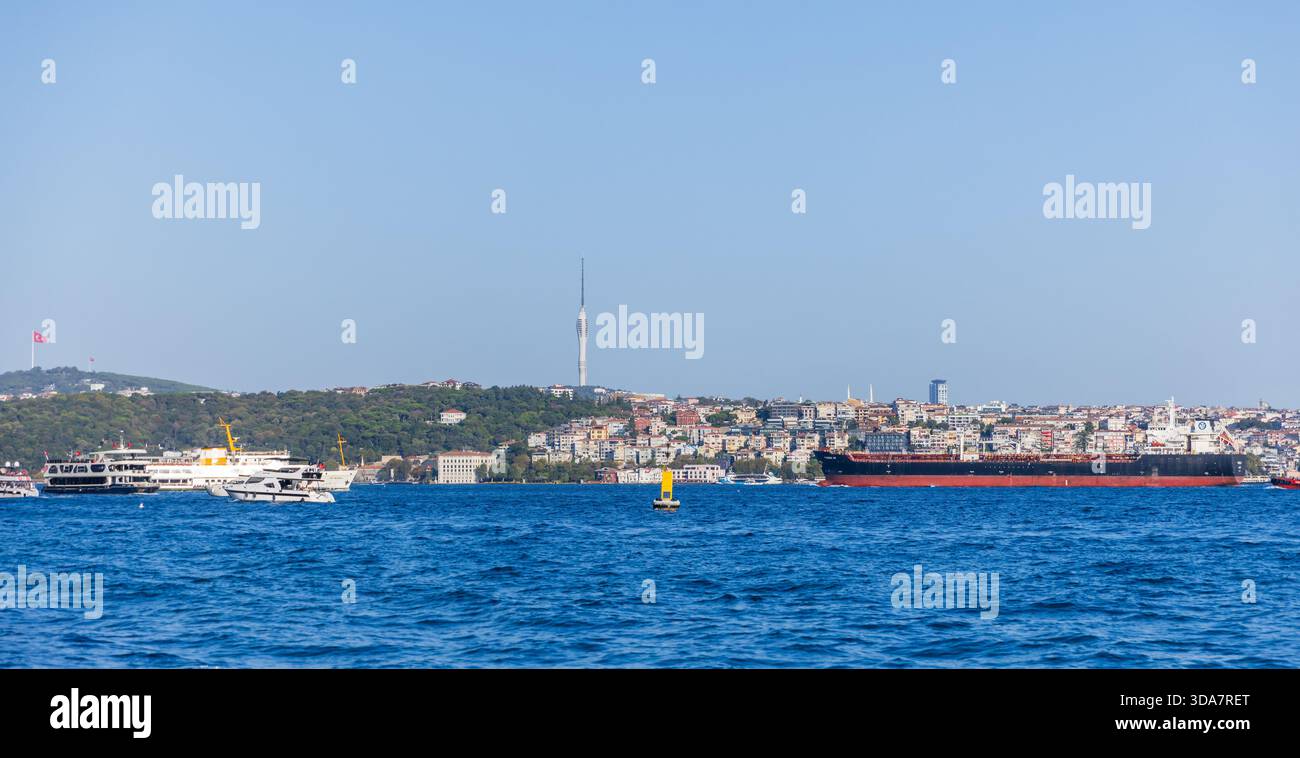 Istanbul, Türkei - 23. August 2025: Ein lebhafter Blick auf den Bosporus zeigt Yachten und ein großes Frachtschiff vor einer Skyline der Küstenstadt Stockfoto