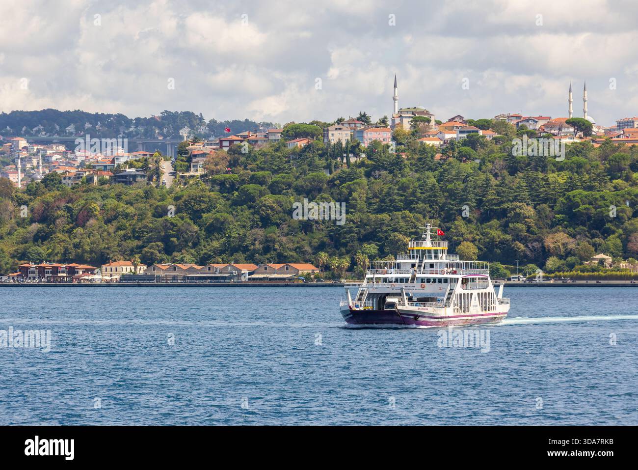 Istanbul, Türkei - 24. August 2025: Eine Fähre mit dem Pkw gleitet über das blaue Bodphorus-Wasser, während ein Hügel mit Bäumen, Minaretten und Ho liegt Stockfoto