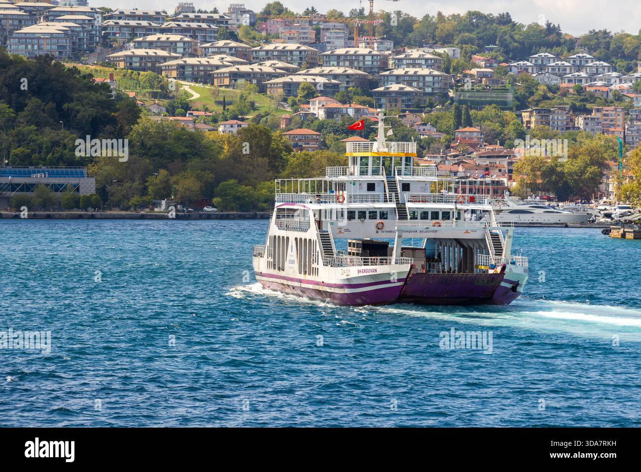 Istanbul, Türkei - 24. August 2025: Eine weiß-violette Passagierfähre gleitet über das leuchtend blaue Bodphorus-Wasser, während ein Hangviertel mit t Stockfoto