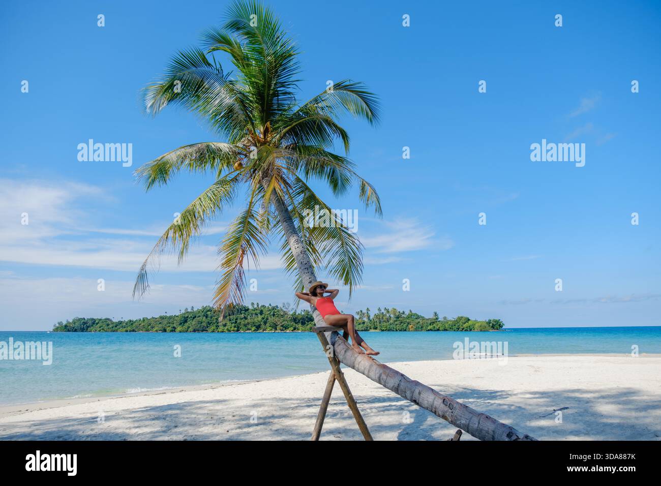 Entspannen Sie unter einer hohen Palme auf Koh Kood Island, eine Frau genießt die ruhige Strandlage. Das klare blaue Wasser und der unberührte Sand schaffen eine perfekte tropische Atmosphäre in Thailand || Model veröffentlicht Stockfoto