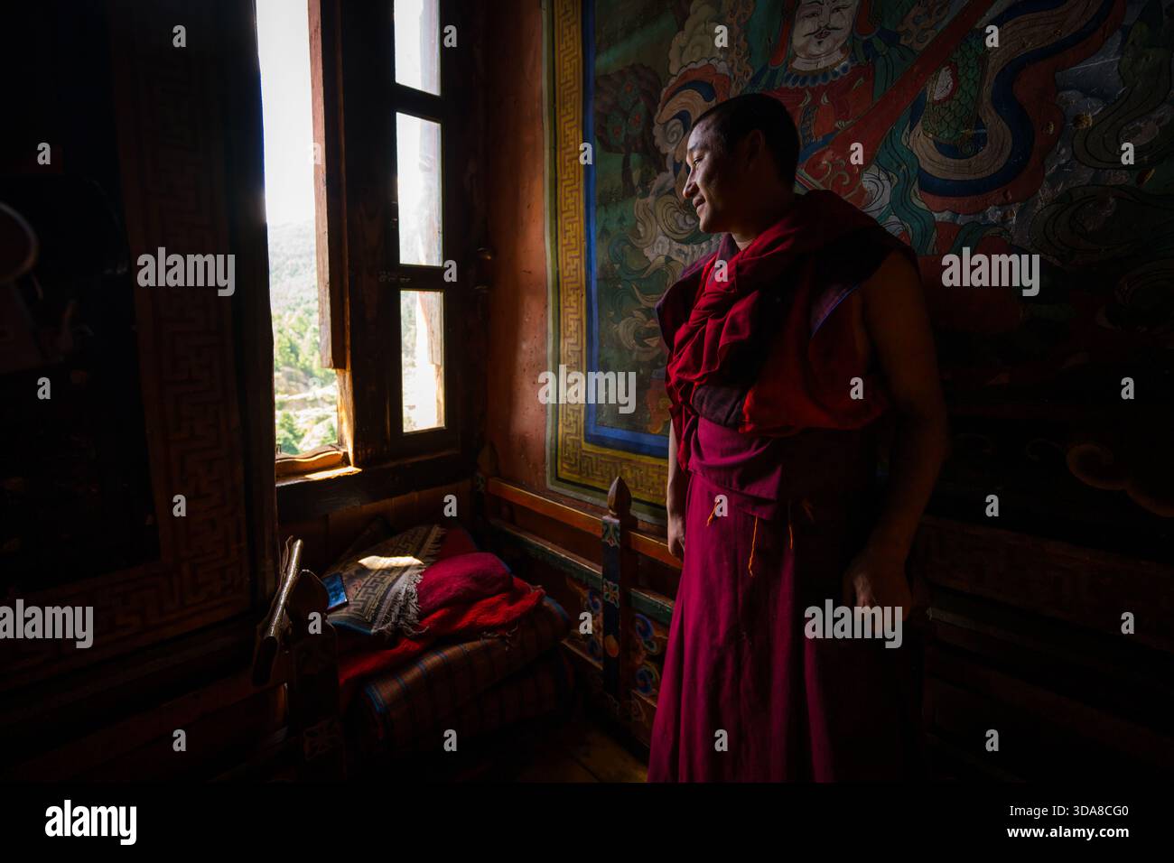 Jakar, Bhutan - 24. September 2025: Blick auf einen Mönch in tiefen kastanienbraunen Gewändern in einem schwach beleuchteten Raum mit bunten Wandgemälden in Dzong, Bumthang. Stockfoto